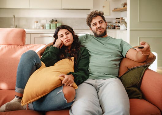 Couple sitting on a couch, holding a remote, and looking bored